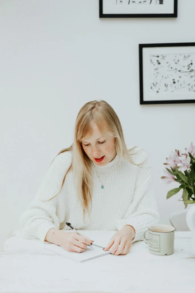 Evie, a makeup artist, wearing a white jumper,looking down as she writes in a notepad