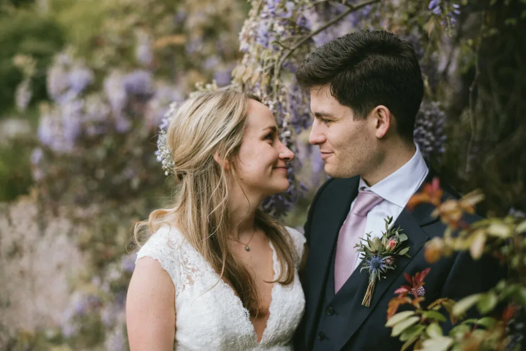A bride and groom smiling at each other in a woodland setting.