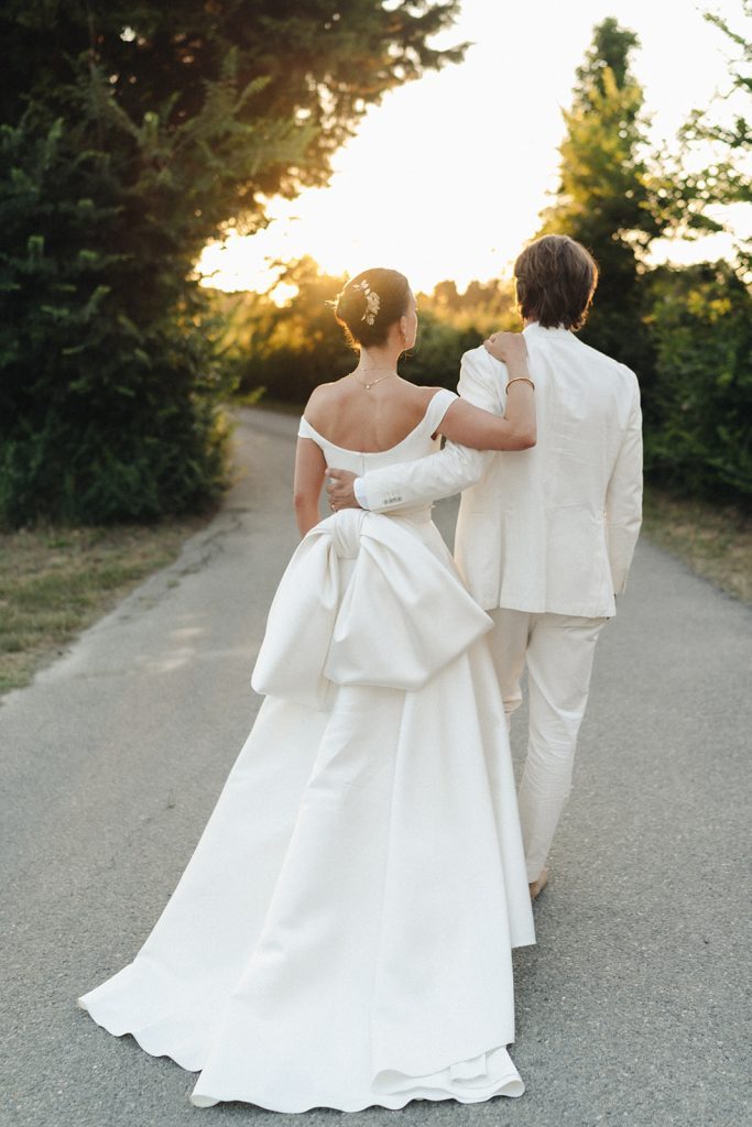 Bride and groom walk together down a path as the sun goes down in the background.