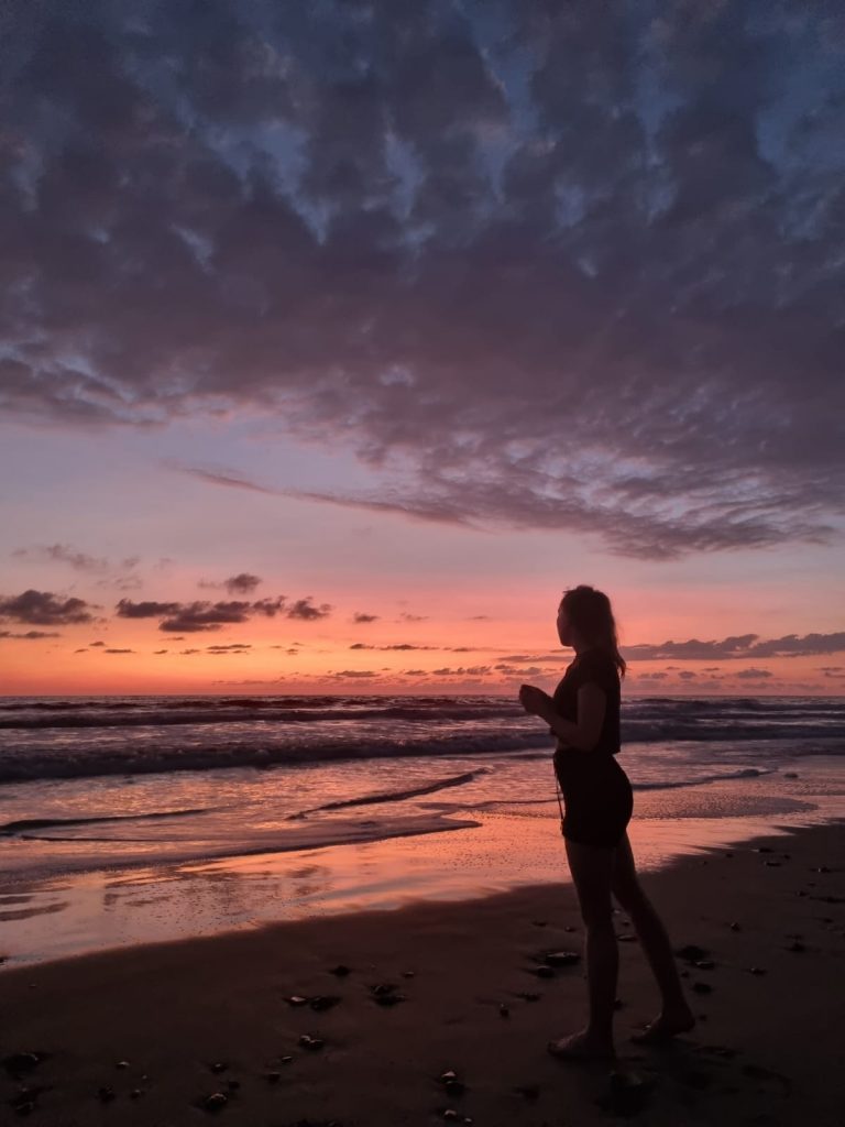Bristol makeup artist Evie Smith standing on a beach at sunset in Costa Rica whilst on location for a commercial makeup shoot.