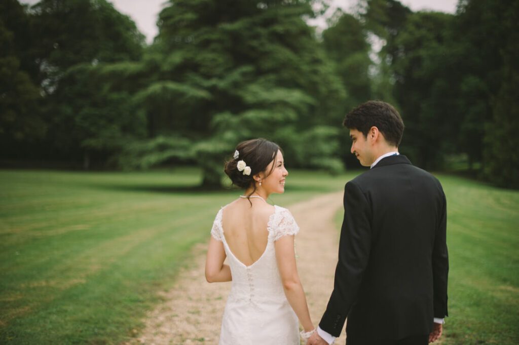 Happy bride and groom walking hand in hand down a track in an orchard.